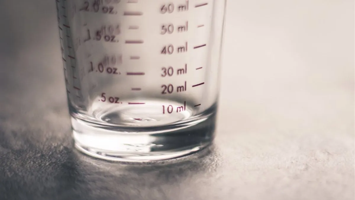 A small glass measuring cup marked in milliliters with a little liquid left in the bottom
