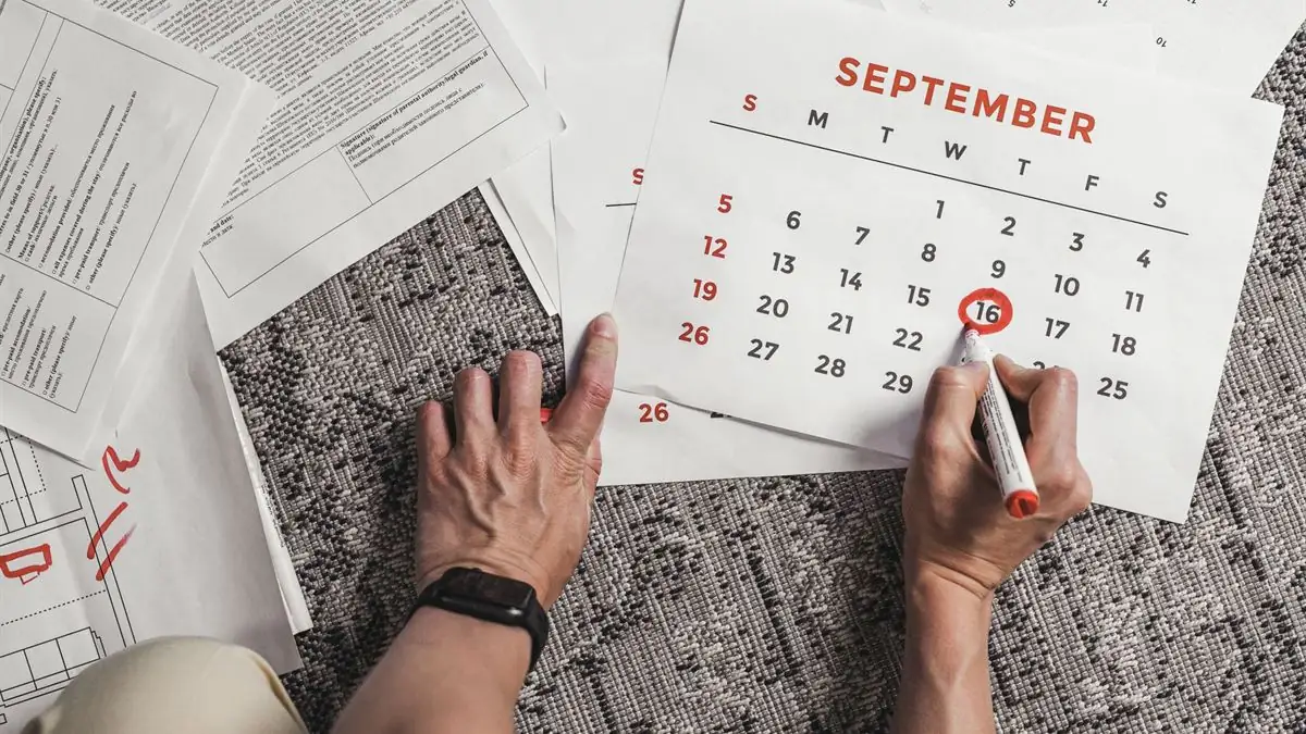 Hands circling a date on a paper calendar in red marker, surrounded by documents