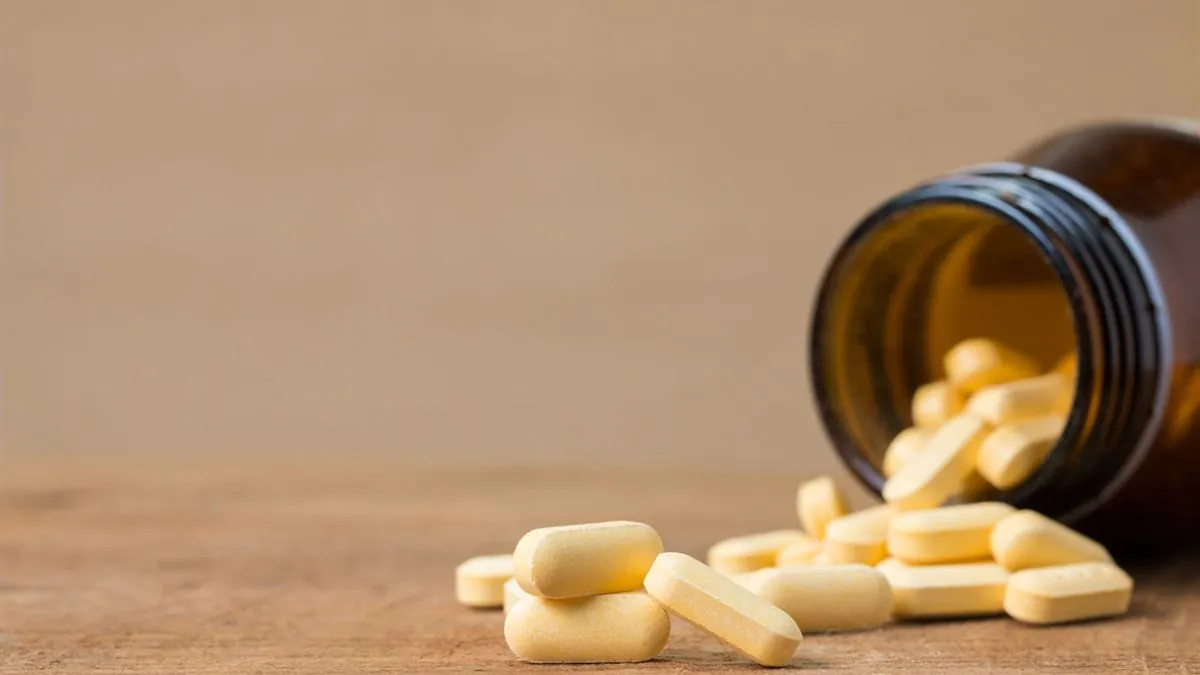 Pale yellow supplement tablets spilling from an amber glass bottle onto a wooden surface