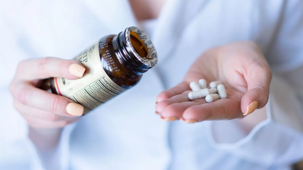 Hands holding a medicine bottle and loose pills, reading the label closely