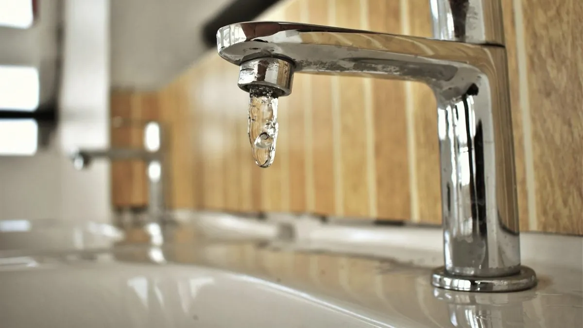 A bathroom tap with a single drop of water hanging from the spout, about to fall